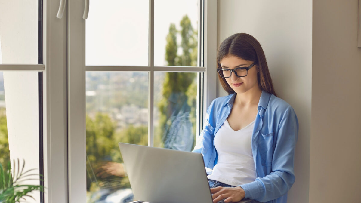 A Young Woman Using A Laptop To Organize Digital Photos In Front Of A Window.