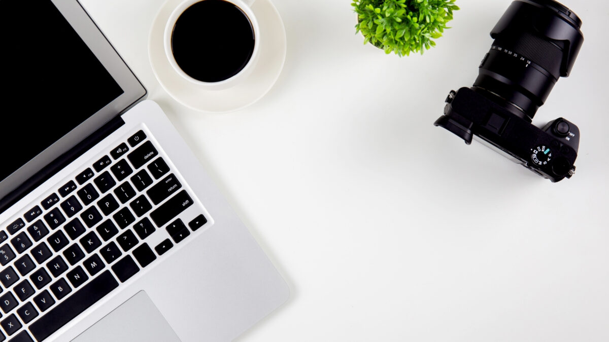 A Laptop With A Camera On A White Table, Perfect For Storing And Backing Up Photos.