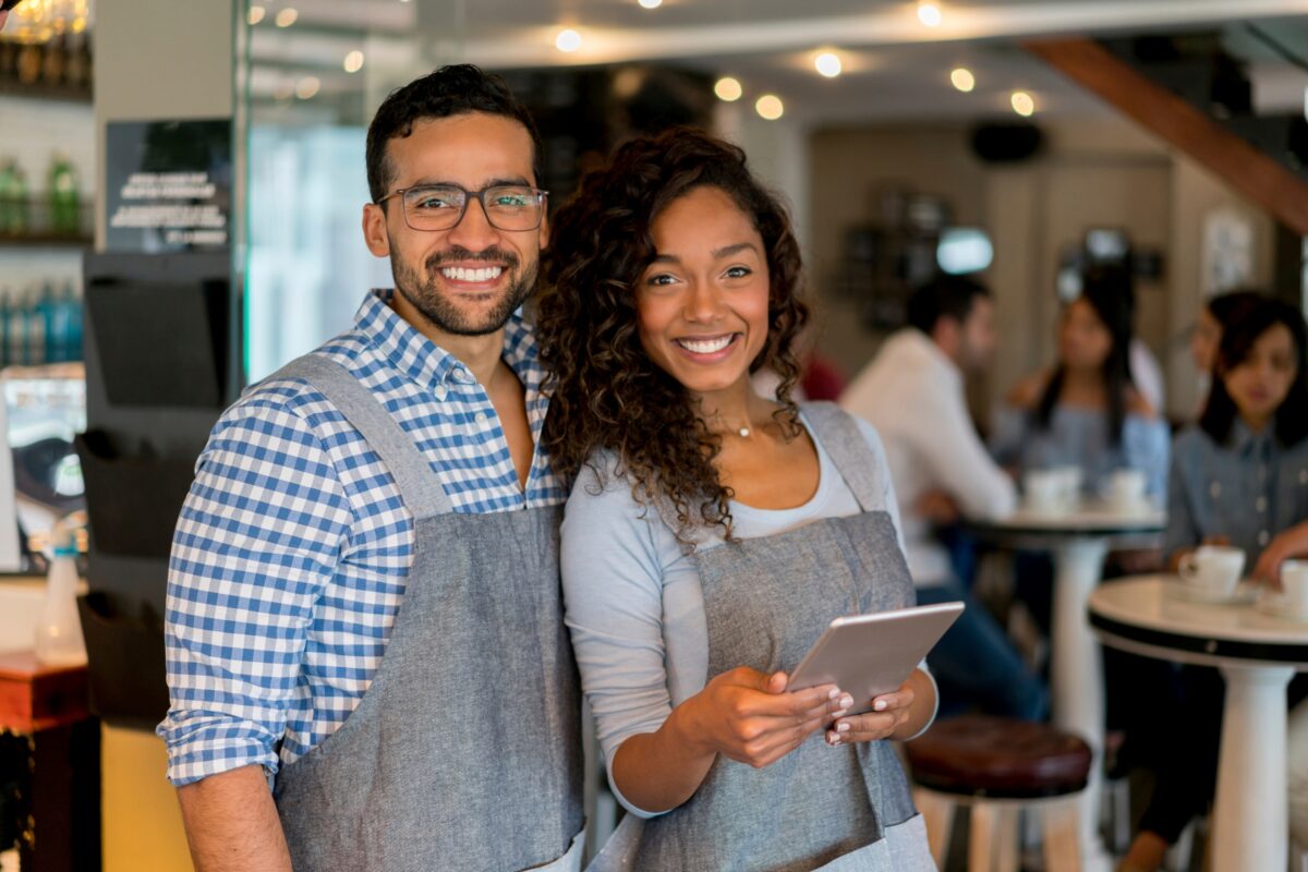 A Smiling Couple In A Restaurant Enjoying Their Meal While Holding A Tablet.