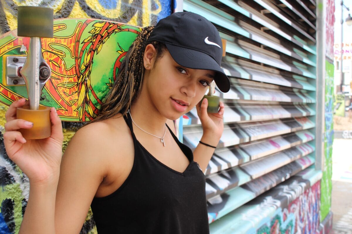 A Woman Holding A Skateboard In Front Of A Graffiti Wall, Suitable For Photography Beginners.