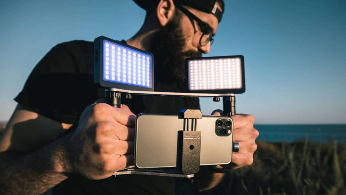 A Bearded Man Capturing Photos With His Smartphone Camera, Equipped With A Light Attachment.
