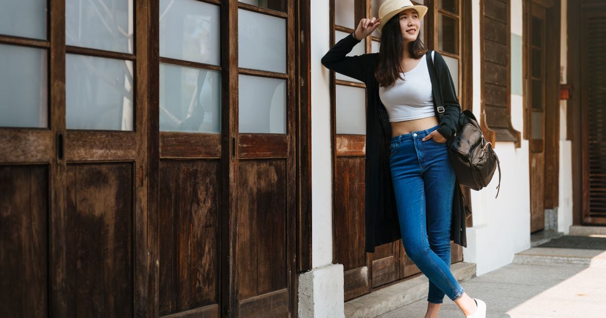Asian Woman Poses For Pictures Leaning Against A Wooden Wall.