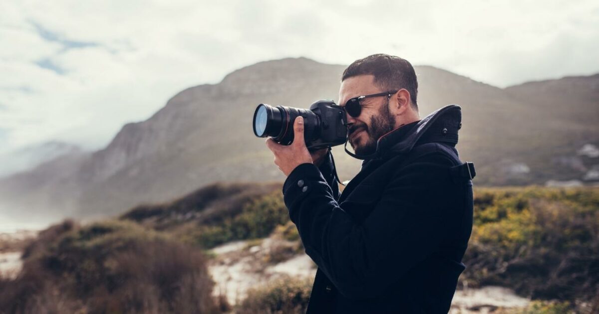 A Man Is Capturing A Picture With His Camera On The Beach For A Photo Essay.