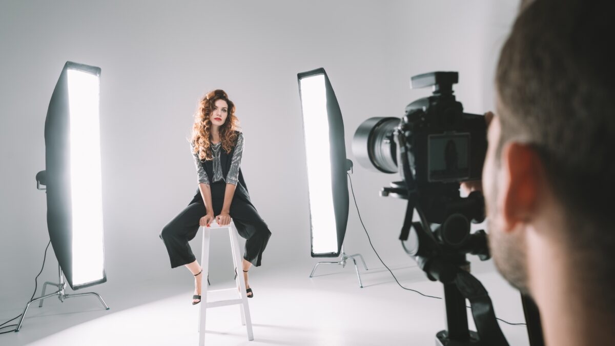 A Woman Is Sitting On A Stool In Front Of A Camera.
