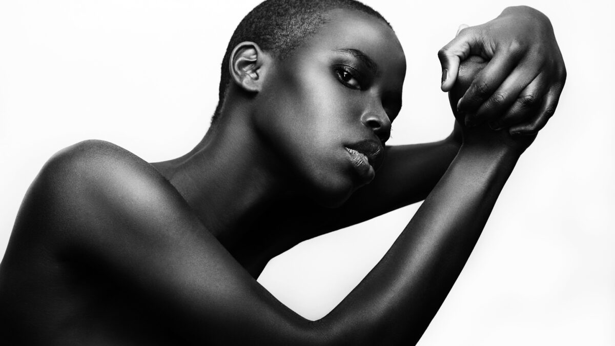 A Black Woman Is Posing In Front Of A White Background, Captured With A Photography Lighting Setup.