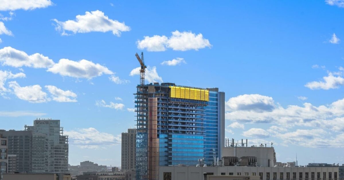 A Captivating Photo Essay Capturing The Essence Of A Building Under Construction Against A Beautiful Blue Sky Adorned With Fluffy Clouds.