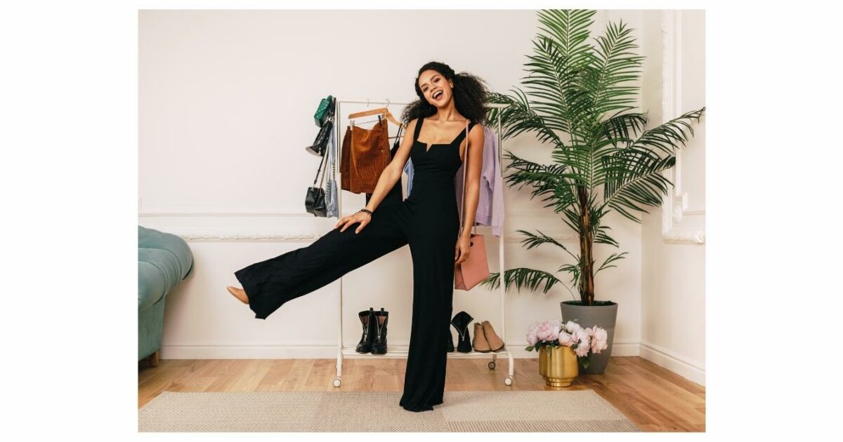 A Woman In A Black Jumpsuit Standing In Front Of A Rack, Showcasing An Ideal Outfit For A Photoshoot.